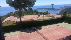 Ein Tennisplatz mit freiem Blick auf das Meer und die umliegenden Gebäude.