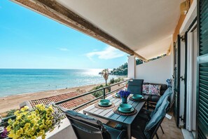 Un balcon avec vue sur la mer, une table avec des assiettes bleues et un vase de fleurs, et un canapé avec des coussins.