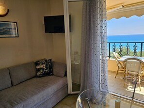 Ein Wohnzimmer mit einer Couch, einem Fernseher und einem Balkon mit Tisch und Stühlen.