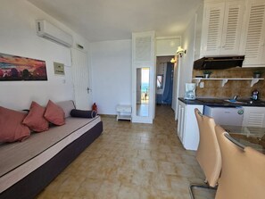 A compact living space with a sofa, kitchenette, and a view through an open door. - Corfu Glyfada Menigos Resort 2-5 (Pelekas)