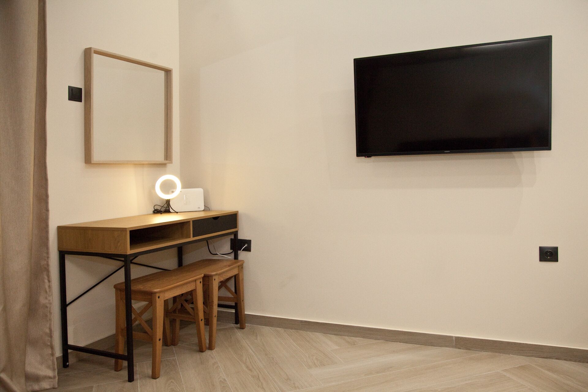 A room with a wooden desk, a mirror, a ring light, and a mounted TV.