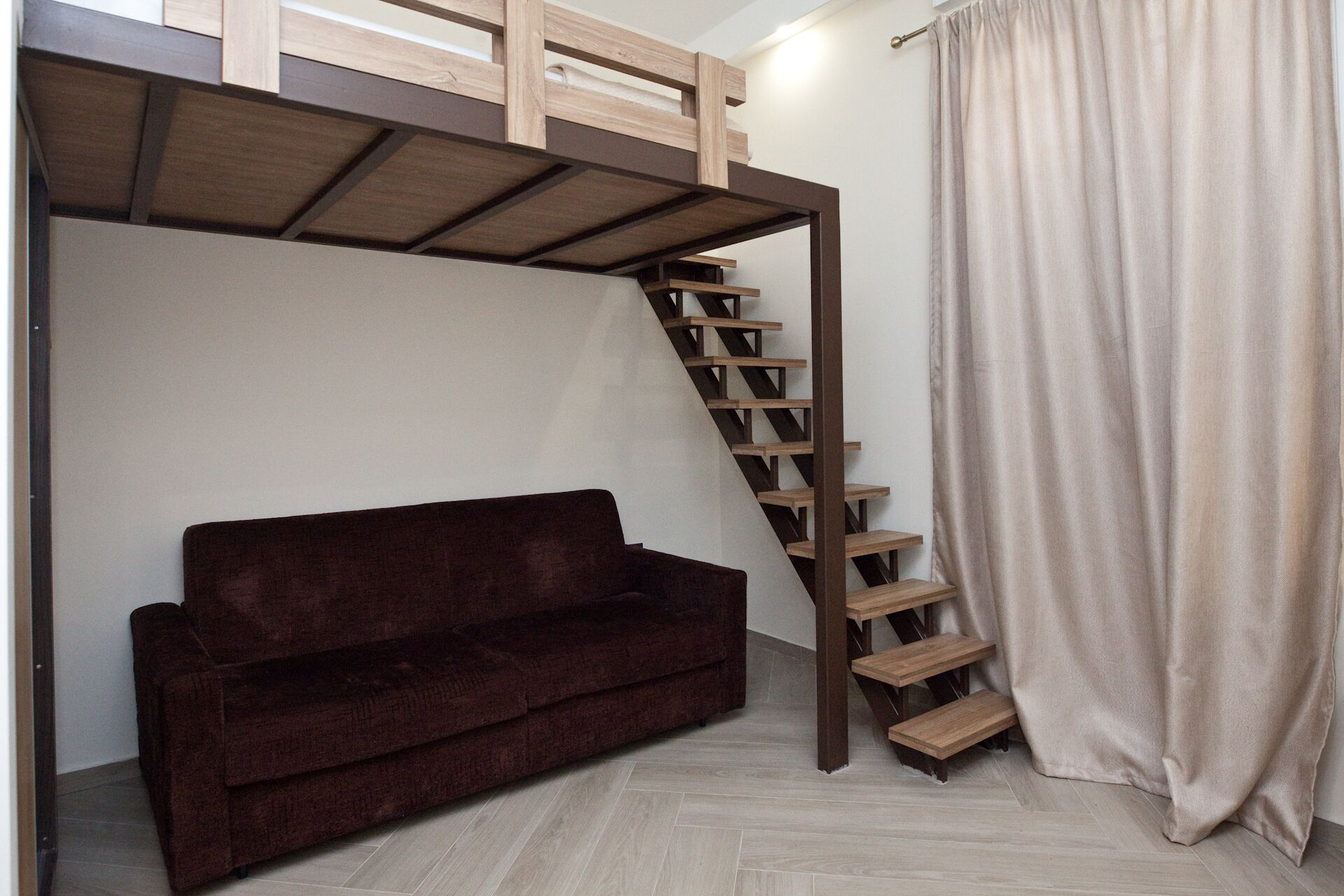 Une pièce avec un lit superposé, un canapé marron et un escalier.