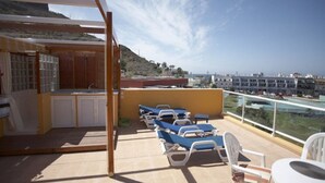A balcony with blue lounge chairs, a small table, and a bar area with a view of the city and hills. - Golden Beach n 12, top floor apartment with private roof terrace by El Sirocco (Lomo Quiebre)