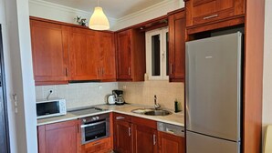 Una cocina con armarios de madera, un refrigerador de acero inoxidable, un microondas, un horno, un lavamanos y una lámpara colgante.