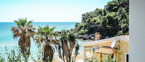 A coastal view with a beach, palm trees, and a building with a tiled roof.