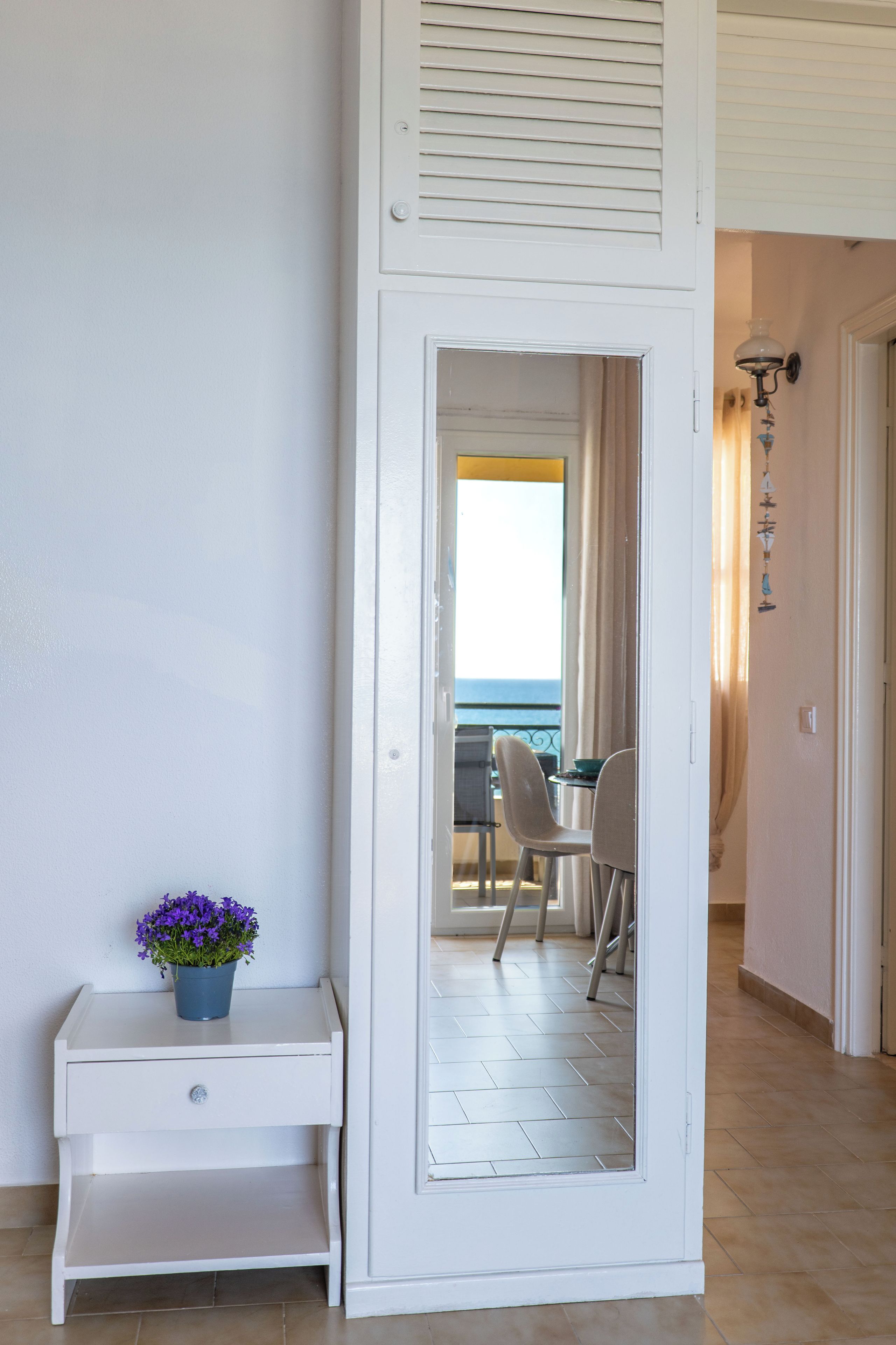 A room with a white door leading to a balcony with a view of the sea.