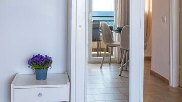 A room with a white door leading to a balcony with a view of the sea.