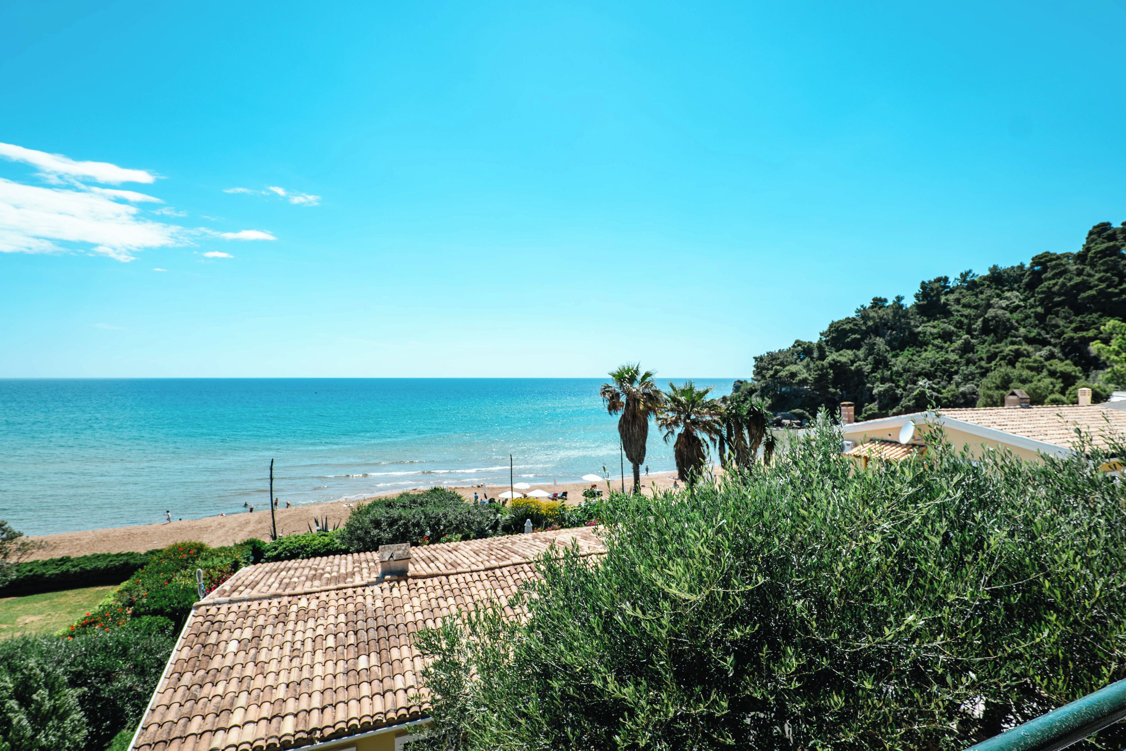 Vista sulla costa con spiaggia, palme e un edificio con tetto in tegole.