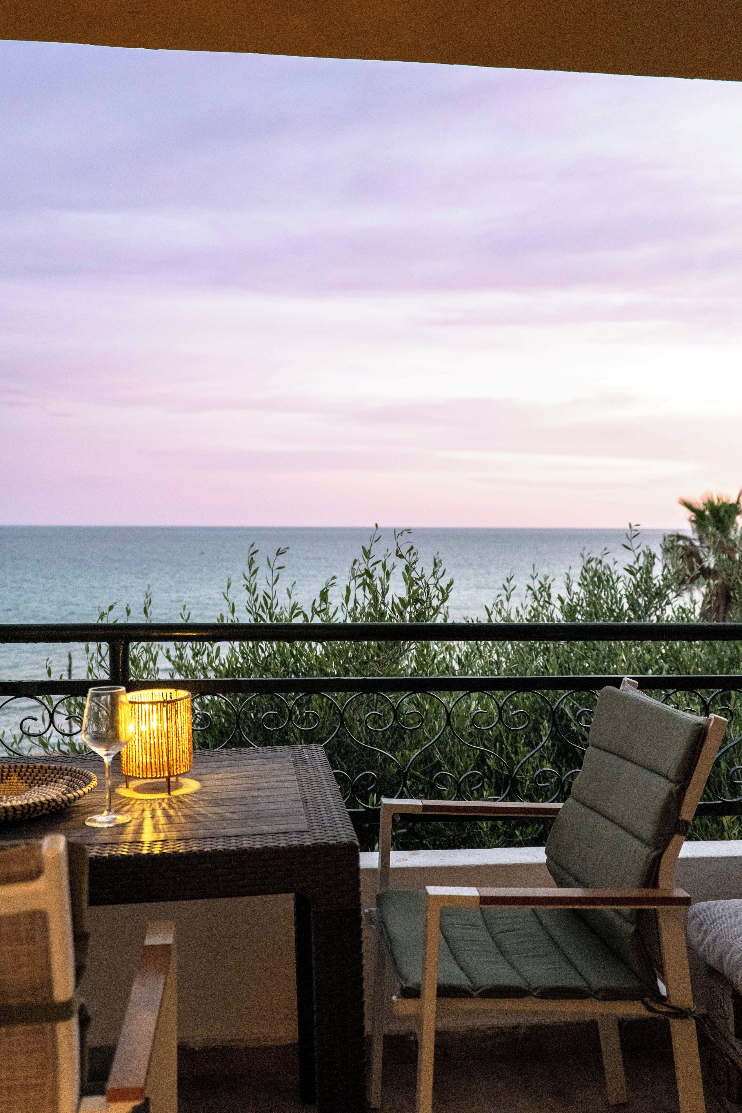 A balcony with a table, a chair, and a view of the sea.
