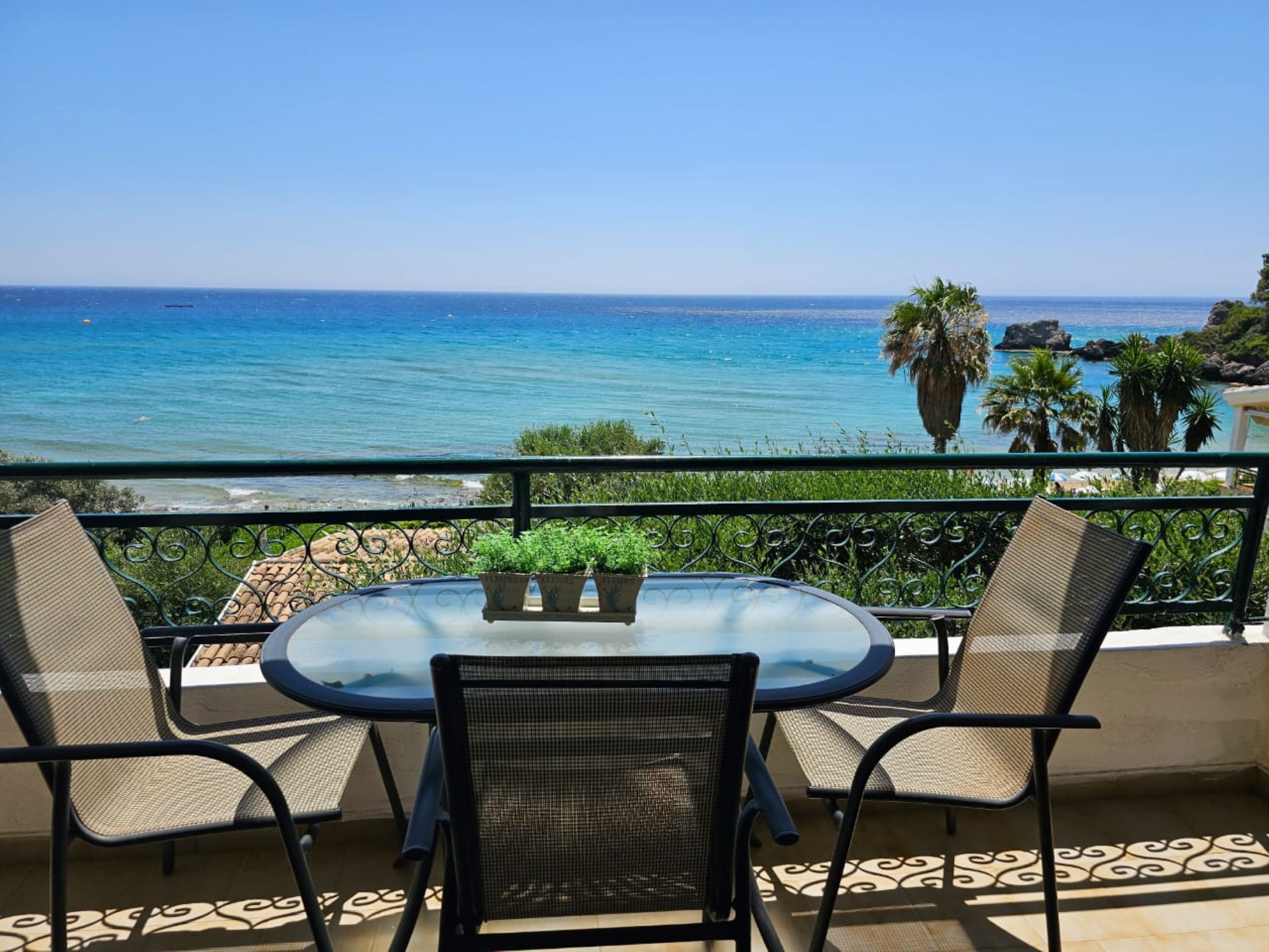 Ein Balkon mit einem runden Tisch und zwei Stühlen, der Blick auf einen Strand und das Meer freigibt.