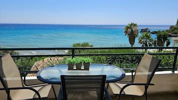Ein Balkon mit einem runden Tisch und zwei Stühlen, der Blick auf einen Strand und das Meer freigibt.