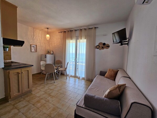 A compact living space with a kitchenette, a dining area, a sofa, and a TV mounted on the wall.