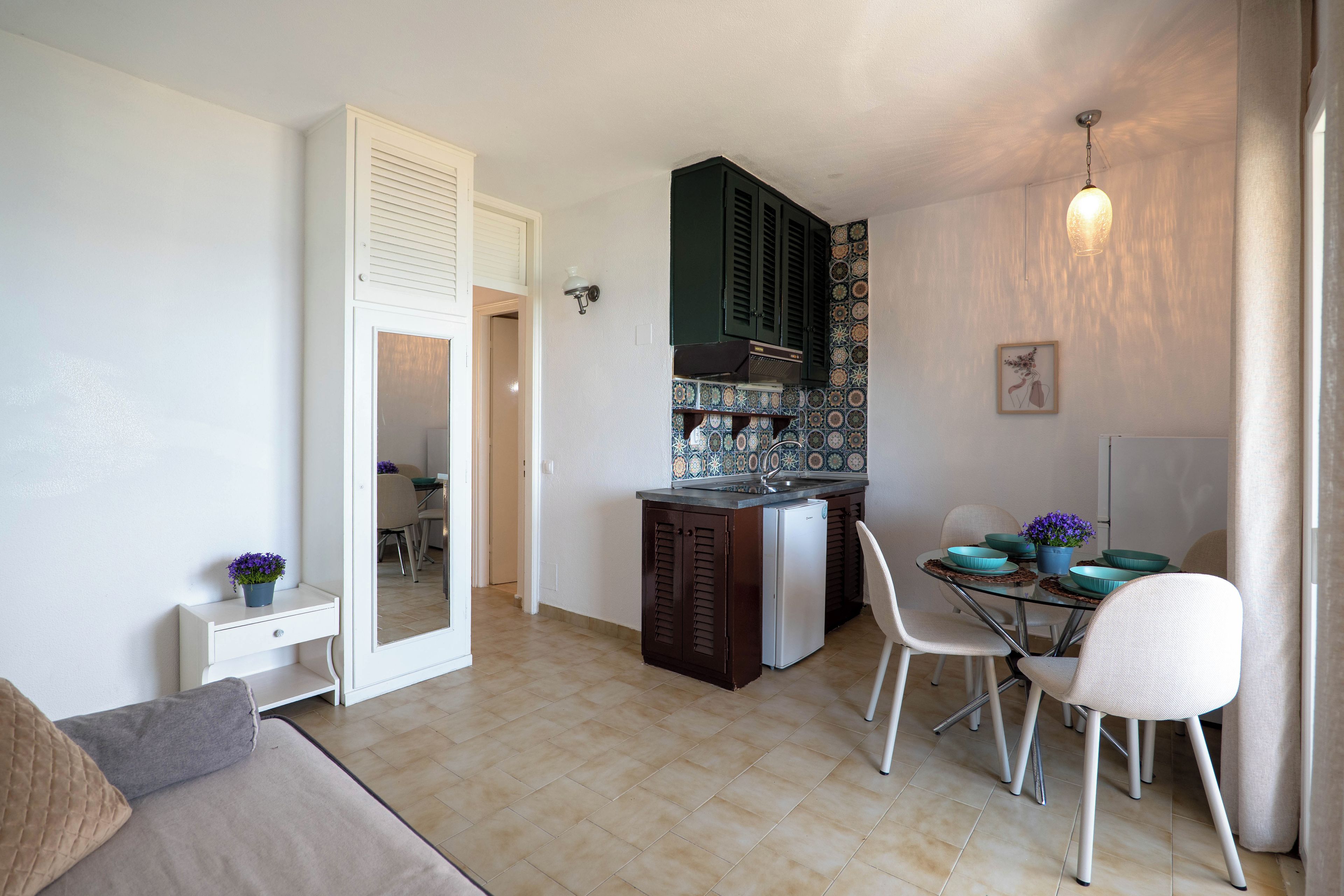 A compact kitchen with a refrigerator, a dining table with chairs, and a small cabinet.