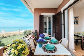 A balcony with a table set for dining, overlooking a beach and the sea.