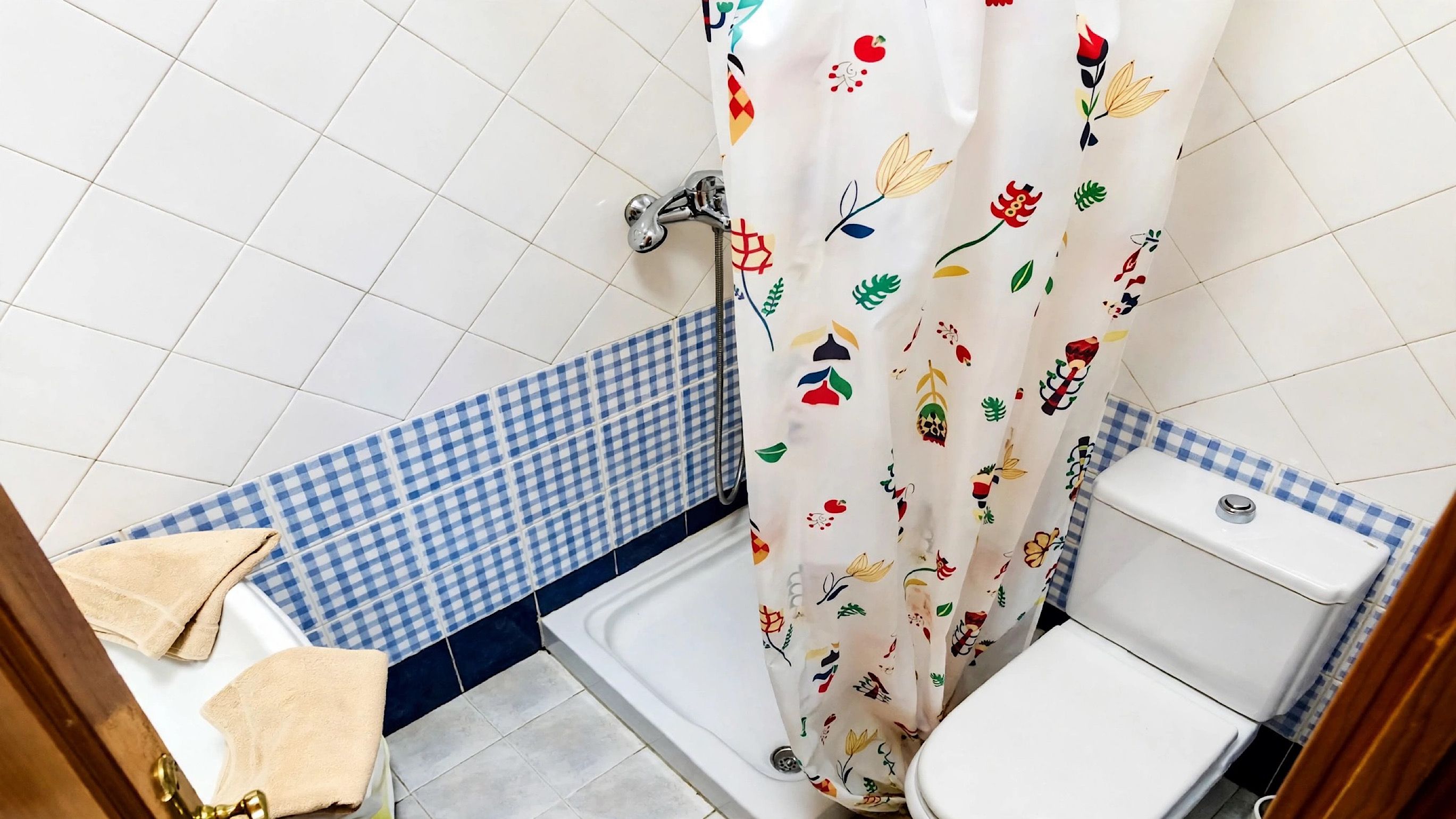 A bathroom with a white toilet, a shower with a floral shower curtain, and a checkered blue and white floor.