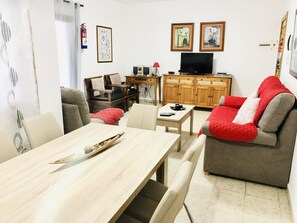 A living room with a dining table, sofa, TV, and wooden cabinets. - Villa Neptuno with private pool, sea view, Smart-TV & free Wifi (Playa Blanca)