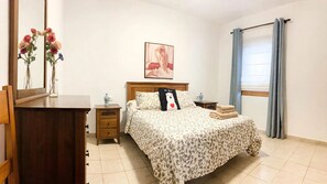 Una camera da letto con un letto, un comodino, una cassettiera, uno specchio, un quadro appeso e una finestra con tende.