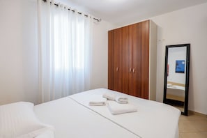 A hotel room with a bed, a wooden wardrobe, a bathroom mirror, and a white curtain.