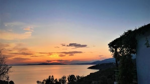 Une vue sur le coucher de soleil, avec un plan d’eau calme, une côte lointaine et de la végétation.