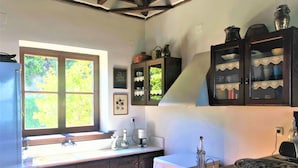 Une cuisine avec des meubles en bois, une fenêtre donnant sur un espace verdoyant, une machine à café et un vase posé sur le plan de travail.