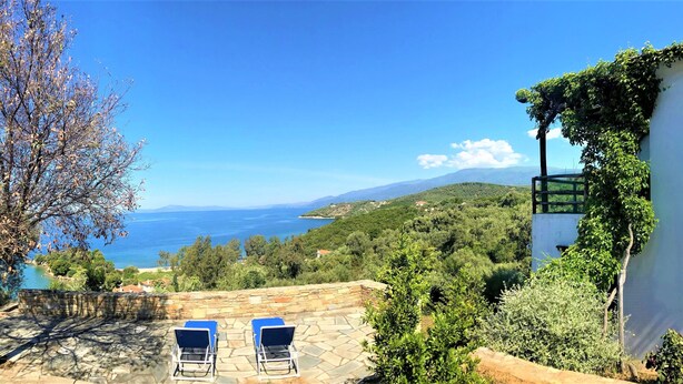 Une terrasse avec deux fauteuils bleus confortables, offrant une vue panoramique sur la mer et les collines.