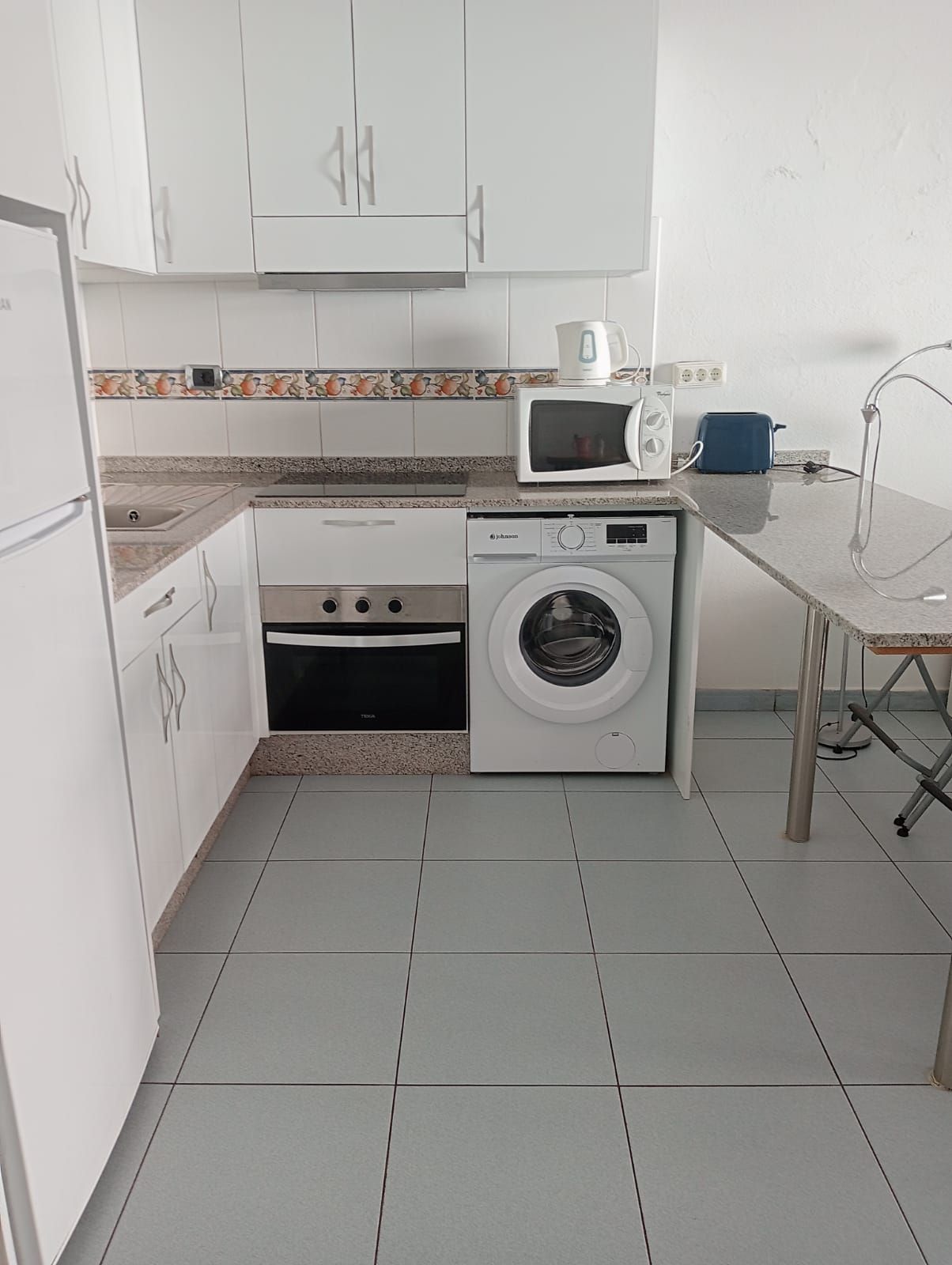 A compact kitchen with white cabinets, a microwave, a toaster, and a washing machine.