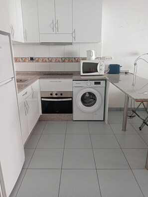 A compact kitchen with white cabinets, a microwave, a toaster, and a washing machine. - Studio Playa Mogan Center (Lomo Quiebre)