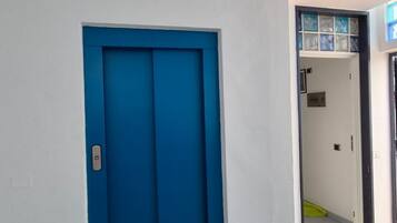 Un couloir avec une porte bleue, un tapis coloré et un sol carrelé.