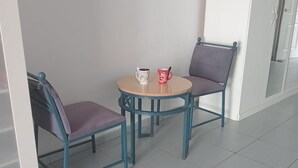 Un coin salon avec deux chaises et une petite table ronde, une plante suspendue au mur et une porte en arrière-plan.
