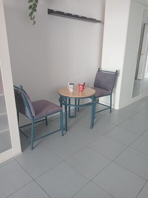 A seating area with two chairs and a small round table, a plant hanging on the wall, and a door in the background.