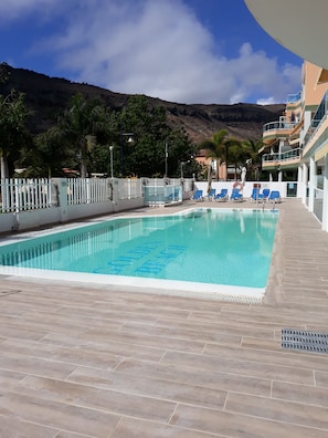 A swimming pool with a clear blue water, surrounded by a tiled deck, and a white fence.