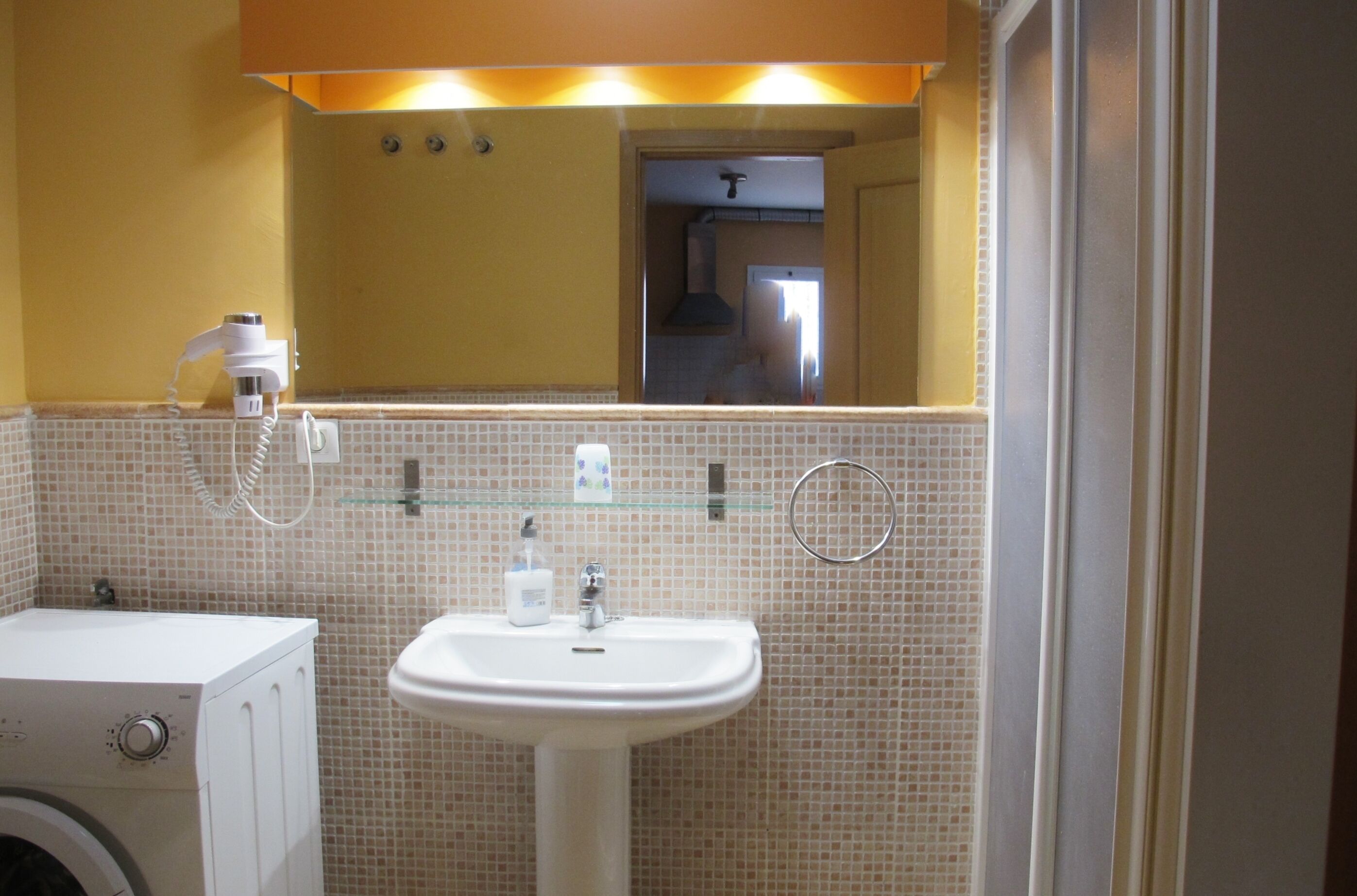 A bathroom with a white sink, a glass shower enclosure, and a washing machine.