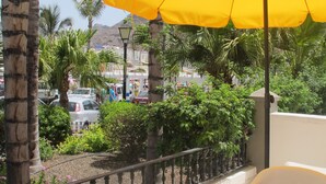 Ein Balkon mit einem gelben Sonnenschirm, Palmen und Blick auf eine belebte Straße mit Autos und Gebäuden.
