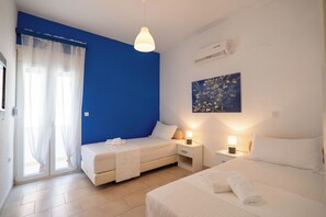 Une chambre d’hôtel avec deux lits, un mur d’accent bleu, un tableau et une fenêtre avec des rideaux légers.