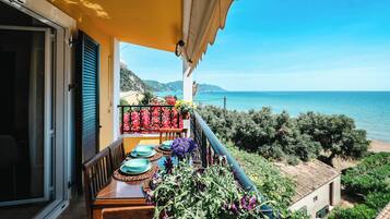 Ein Balkon mit Esstisch, der Blick auf eine Küstenlandschaft mit Bergen und dem Meer bietet.