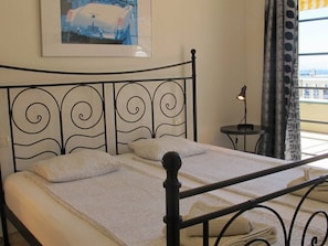 A bed with a metal headboard, a bedside table with a lamp, and a window with curtains.