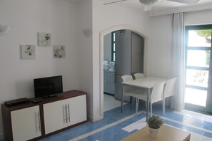 Una habitación con una televisión sobre un mueble, una mesa de comedor con sillas y una planta sobre una mesa.