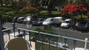 Un balcon avec une chaise et une table, donnant sur un parking où se trouvent des voitures et des palmiers.