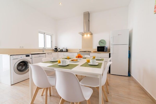 A modern kitchen with a dining table, chairs, a washing machine, and a refrigerator.