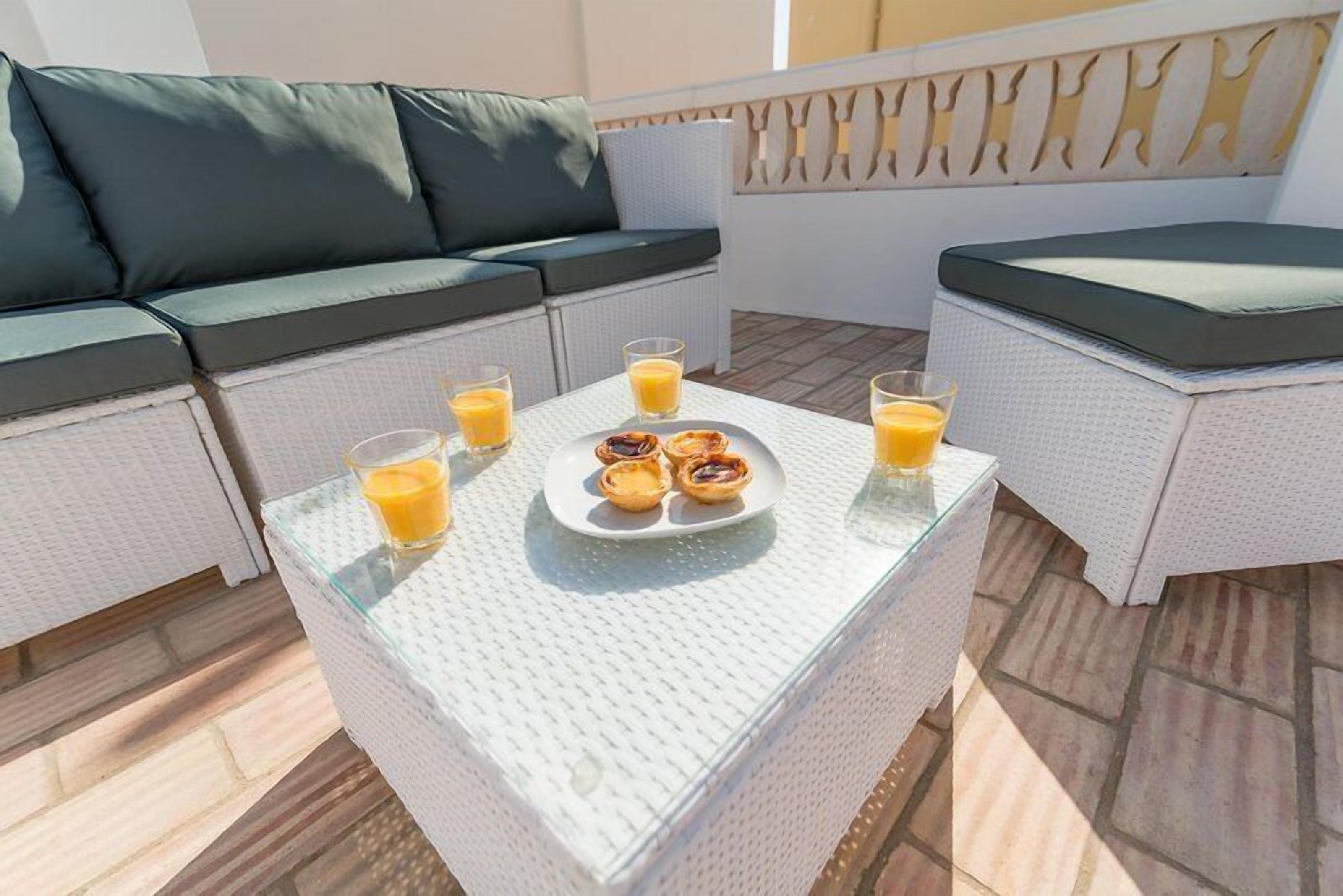 A patio area with a white wicker sofa and a glass table set with orange juice and pastries.