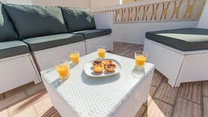 Ein Patio mit einer weißen Rattan-Couch und einem Glastisch, gedeckt mit Orangensaft und Gebäck.