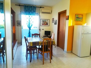 A dining area with a table, chairs, a television, and a refrigerator.