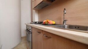 A kitchen with a stainless steel sink, wooden cabinets, and a countertop with fruits. - In Good Location And With Balcony - Casa Vacanze Nicole In Salento (Otranto)