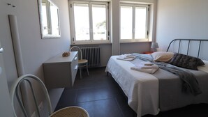 Un dormitorio con cama, escritorio, silla y dos ventanas.