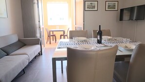 Un comedor con una mesa dispuesta para cuatro personas, un sofá y un televisor montado en la pared.
