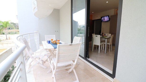 Een balkon met witte stoelen en een tafel, een eethoek met stoelen en een televisie, en uitzicht op de omgeving.