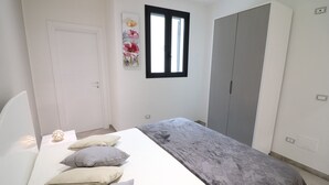 Een slaapkamer met een bed, kussens, een kledingkast en een raam.