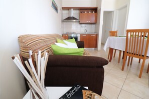 Ein Wohnzimmer mit einer Couch, einem Esstisch und einer Küche im Hintergrund.