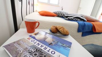 Uma cama com almofadas, um prato com croissants, uma caneca e uma revista sobre uma mesa.