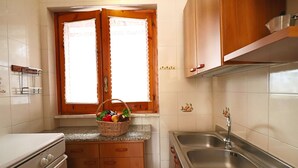 A kitchen with wooden cabinets, a granite countertop, a stainless steel sink, and a window with a lace curtain. - Nice House Cecilia in Otranto (Otranto)